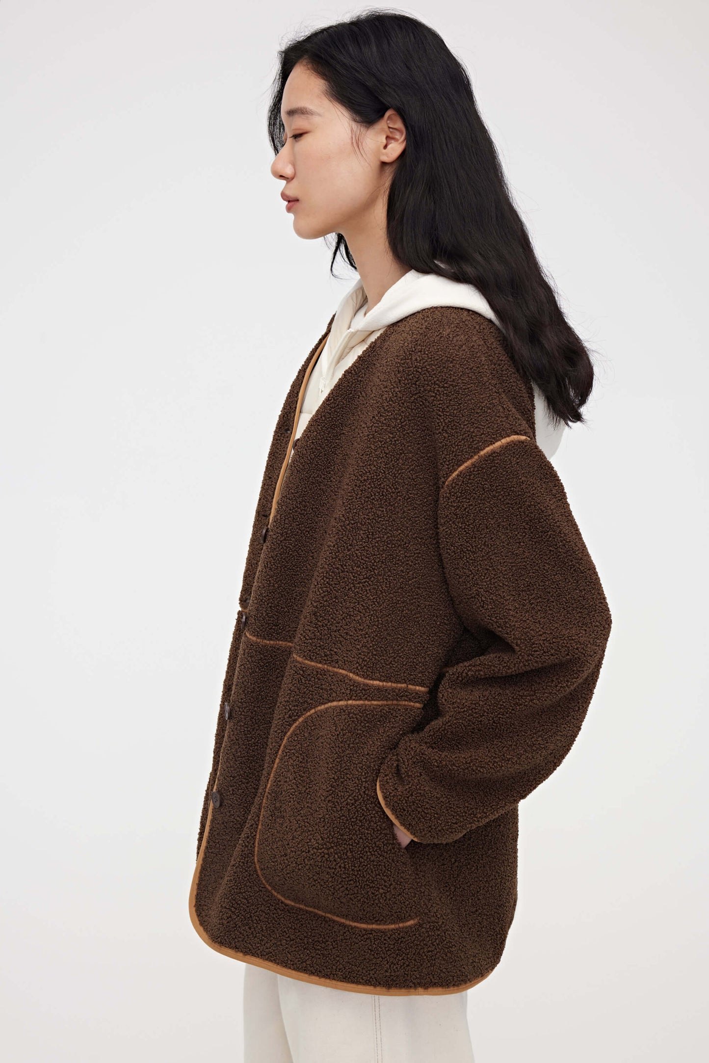 Woman wearing dark brown teddy fleece jacket and facing left
