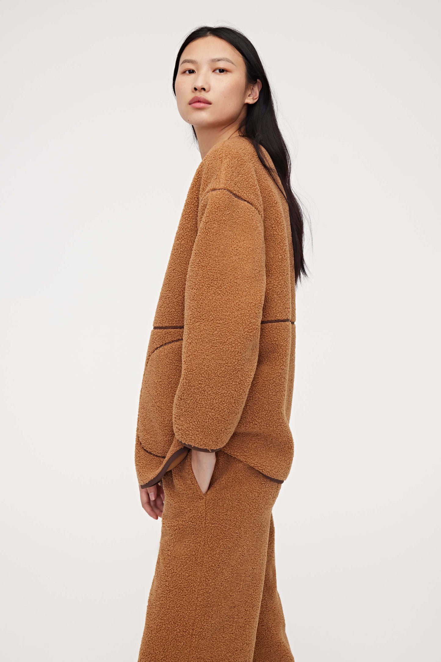 Woman wearing brown teddy fleece jacket and facing left