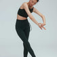a woman doing a dance pose wearing a crew neck dark green sports bra with pleats details and a pair of matching leggings with double layered waist and side knot.