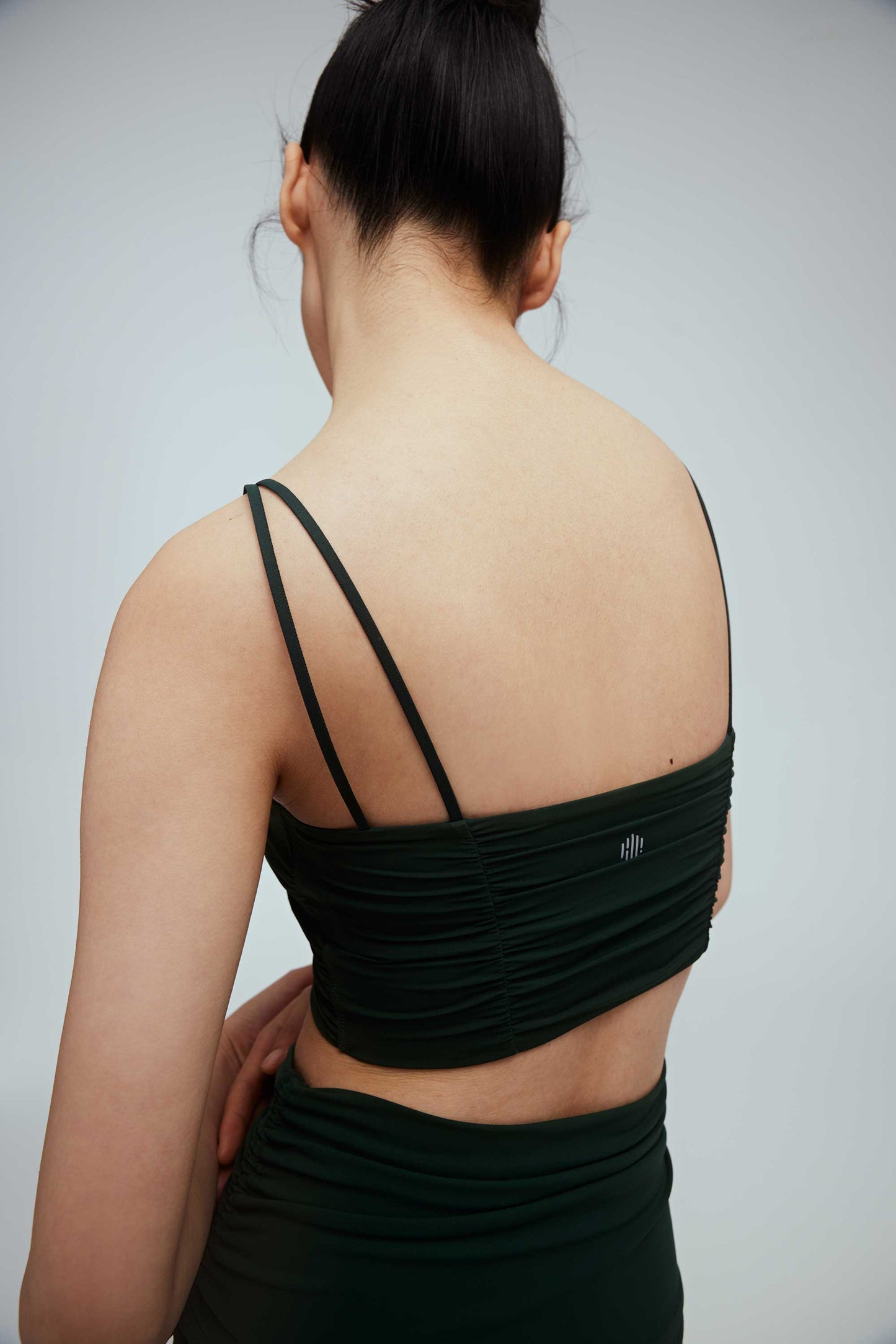 the back a woman wearing a dark green double strap sports bra with pleats details