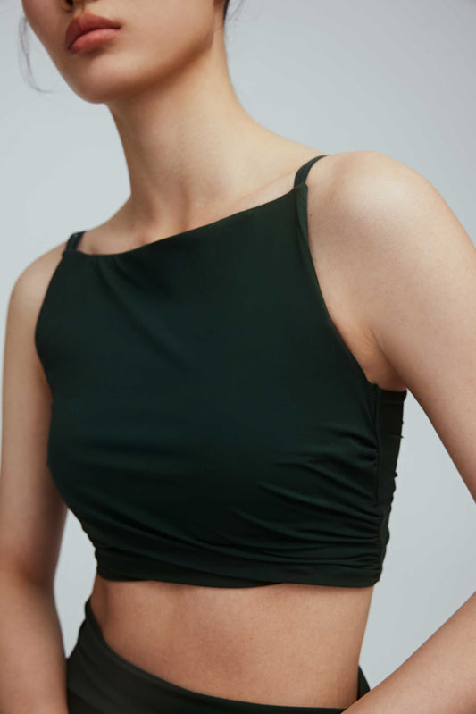 A close look of a woman wearing a crew neck dark green sports bra with pleats details.