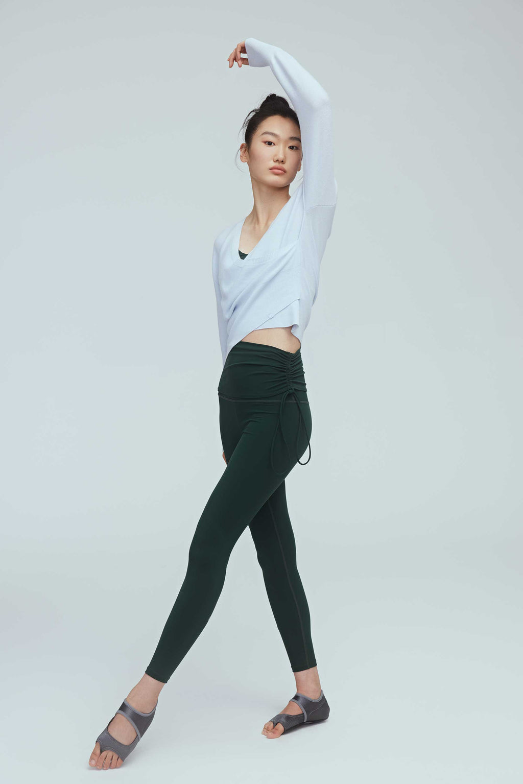 a woman wearing a blue wrap sweater and green leggings.