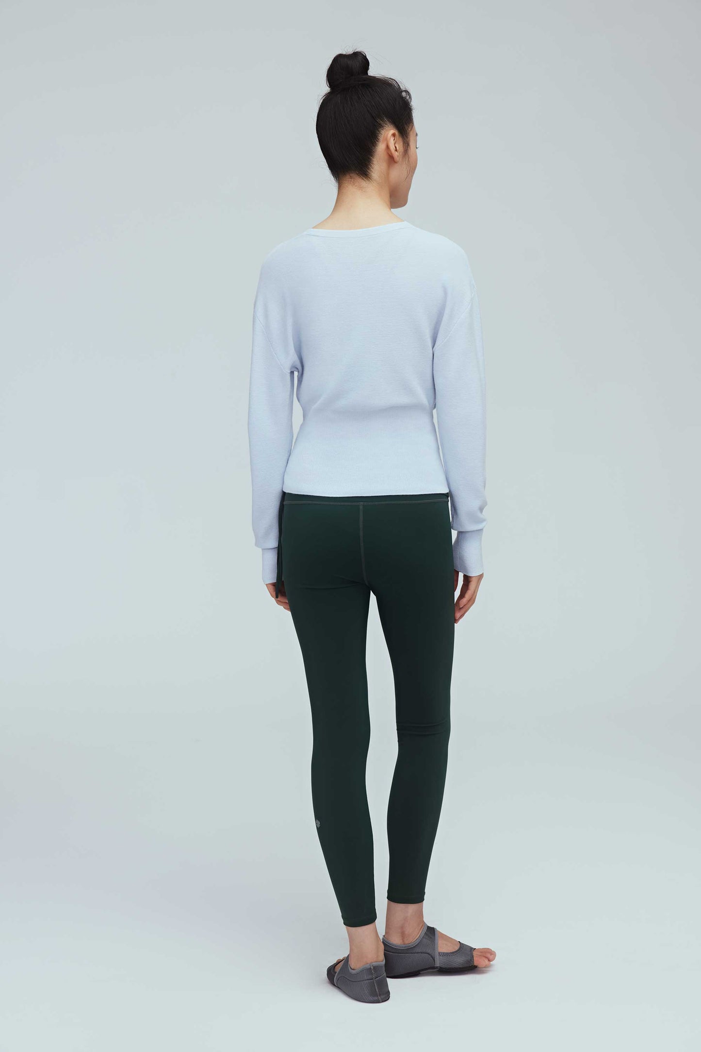 back of a woman wearing a blue wrap sweater and green leggings.