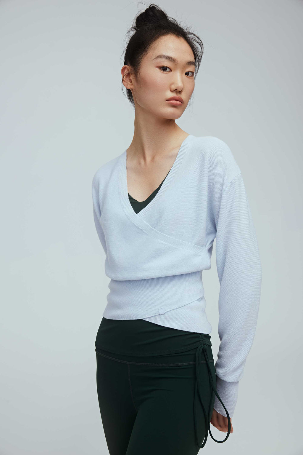 a woman wearing a blue wrap sweater and green leggings.