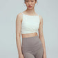 a woman wearing a crew neck white sports bra with pleats details and a pair of grey leggings with double layered waist.