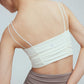 the back of a woman wearing a white sports bra with pleats details and a pair of grey leggings with double layered waist.
