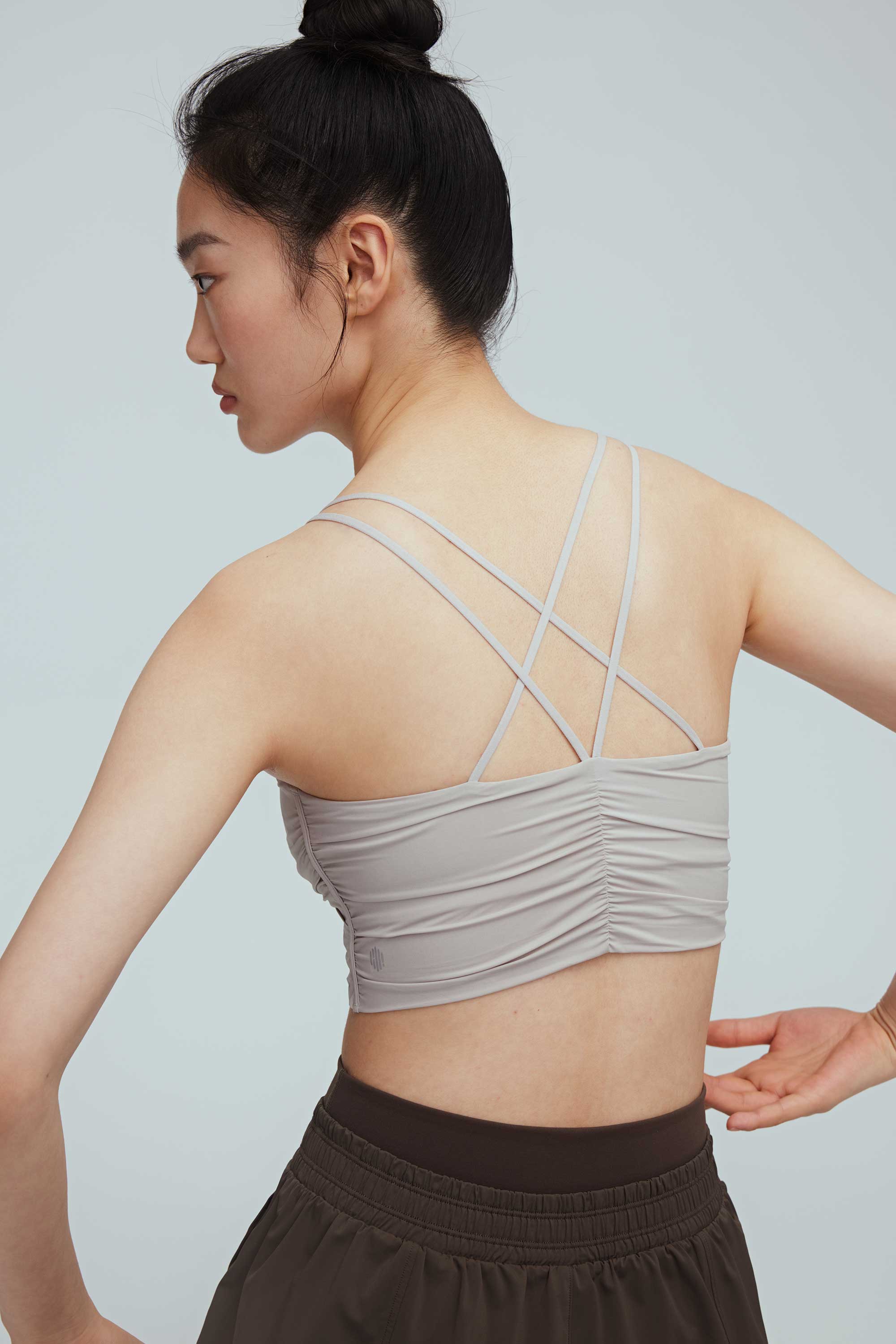 the back of a woman wearing a light grey sports bra with back crossing straps details
