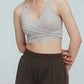 a woman wearing a light grey color v-neck sports bra with ruched details and  a pair of black leggings layered with black shorts 