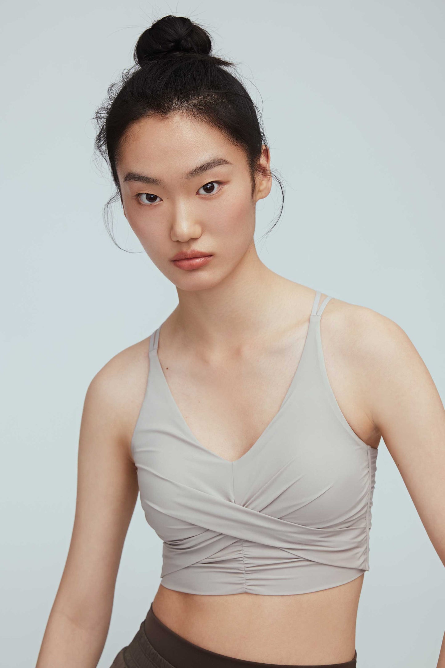 a woman wearing a light grey color v-neck sports bra with ruched details