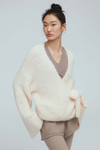 a woman wearing a white wool wrap cardigan and light grey leggings.