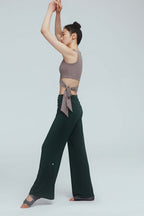side of a woman wearing a light brown wrap bra top and green leggings