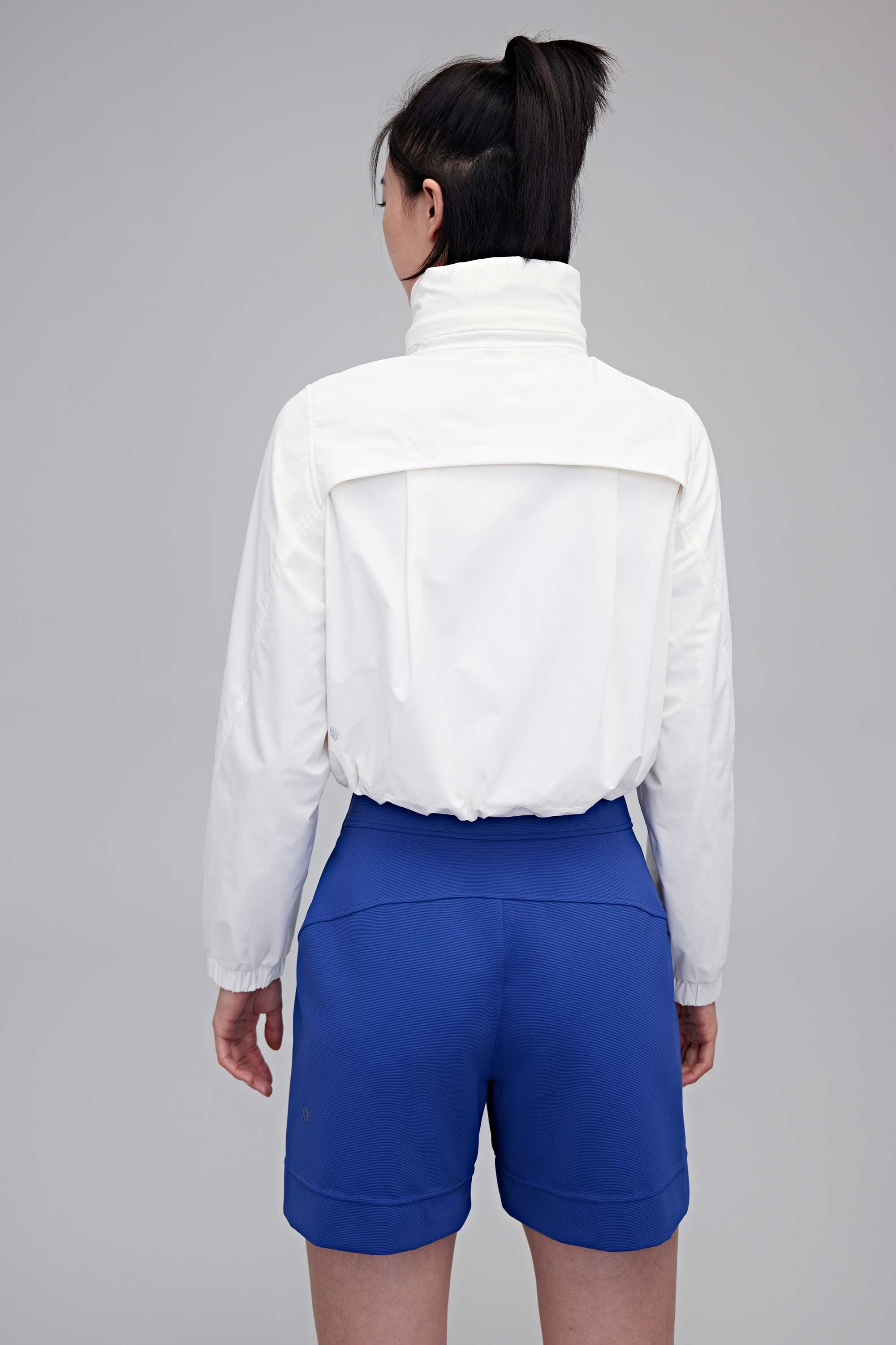 Back of woman in white jacket and blue shorts