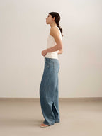 side of a woman wearing a white tank and blue jeans
