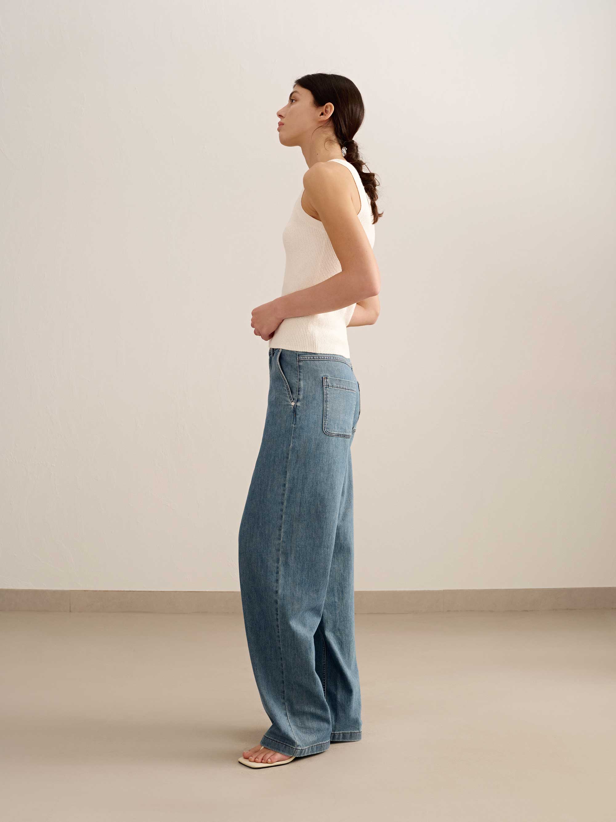 side of a woman wearing a white tank and blue jeans