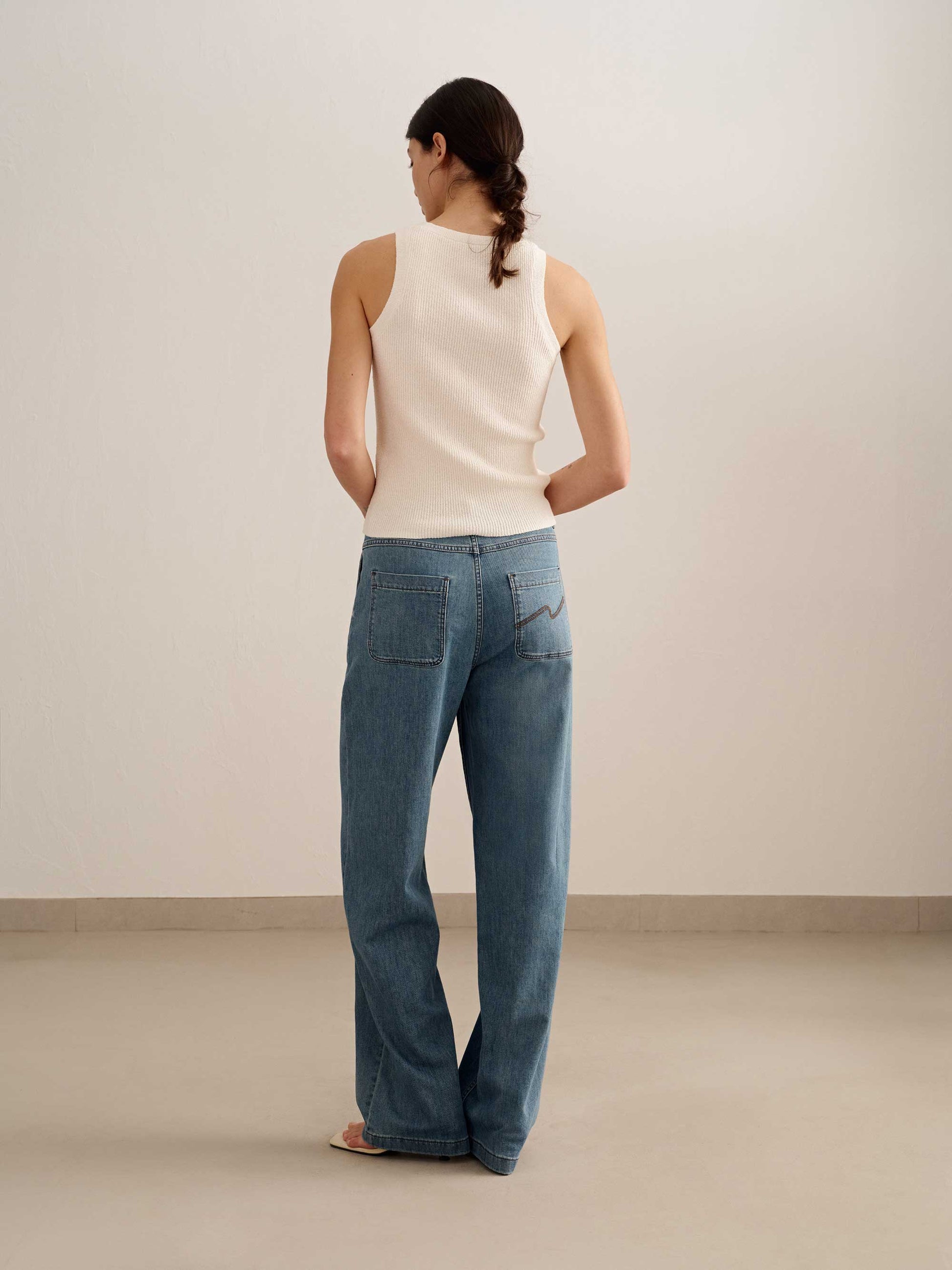 back of a woman wearing white tank and blue jeans