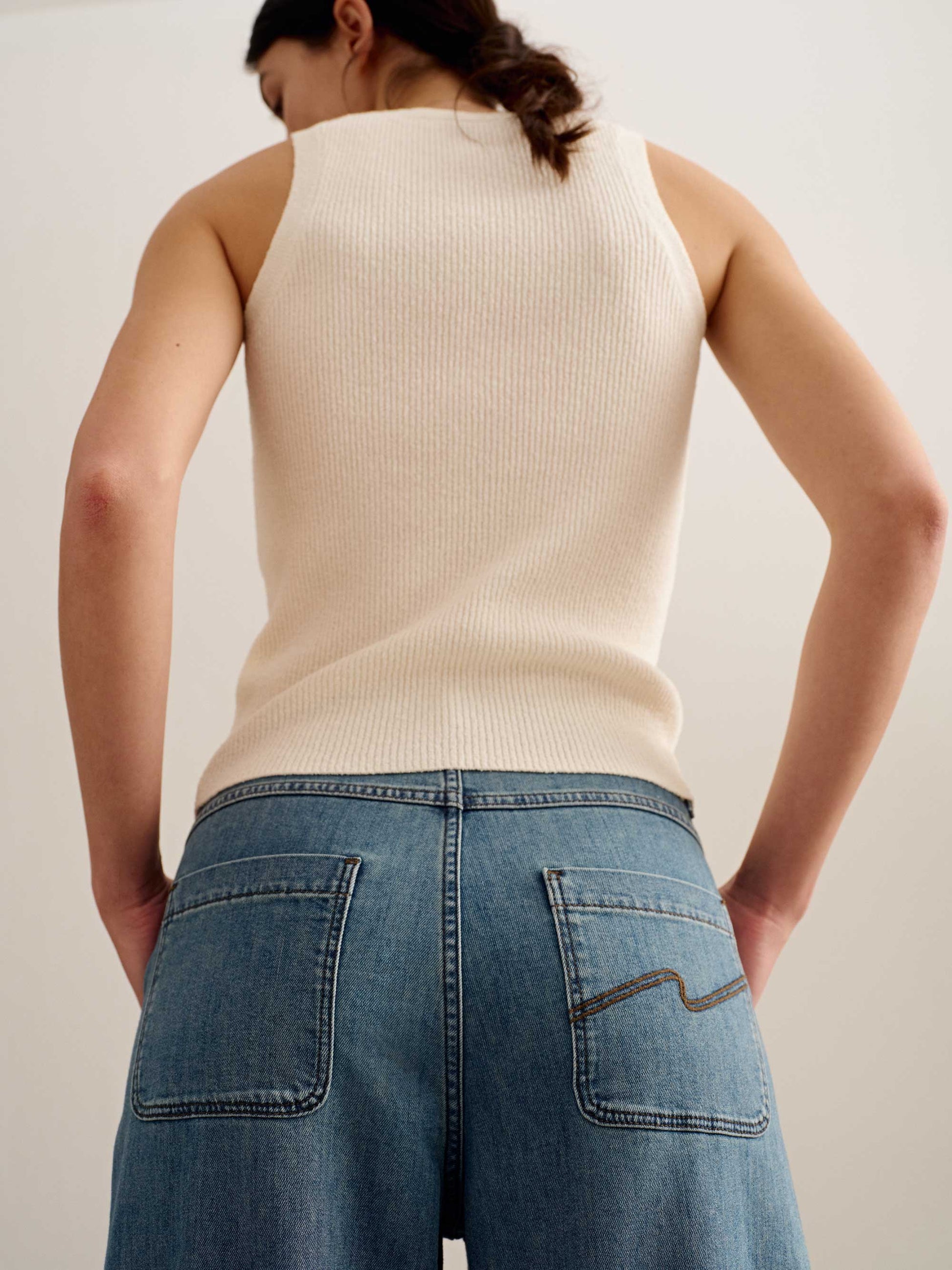 back of a woman wearing a white tank and blue jeans