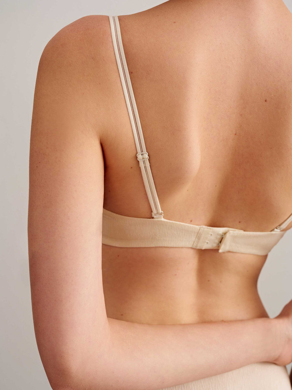 back of a woman wearing a light beige bra with clasp. 
