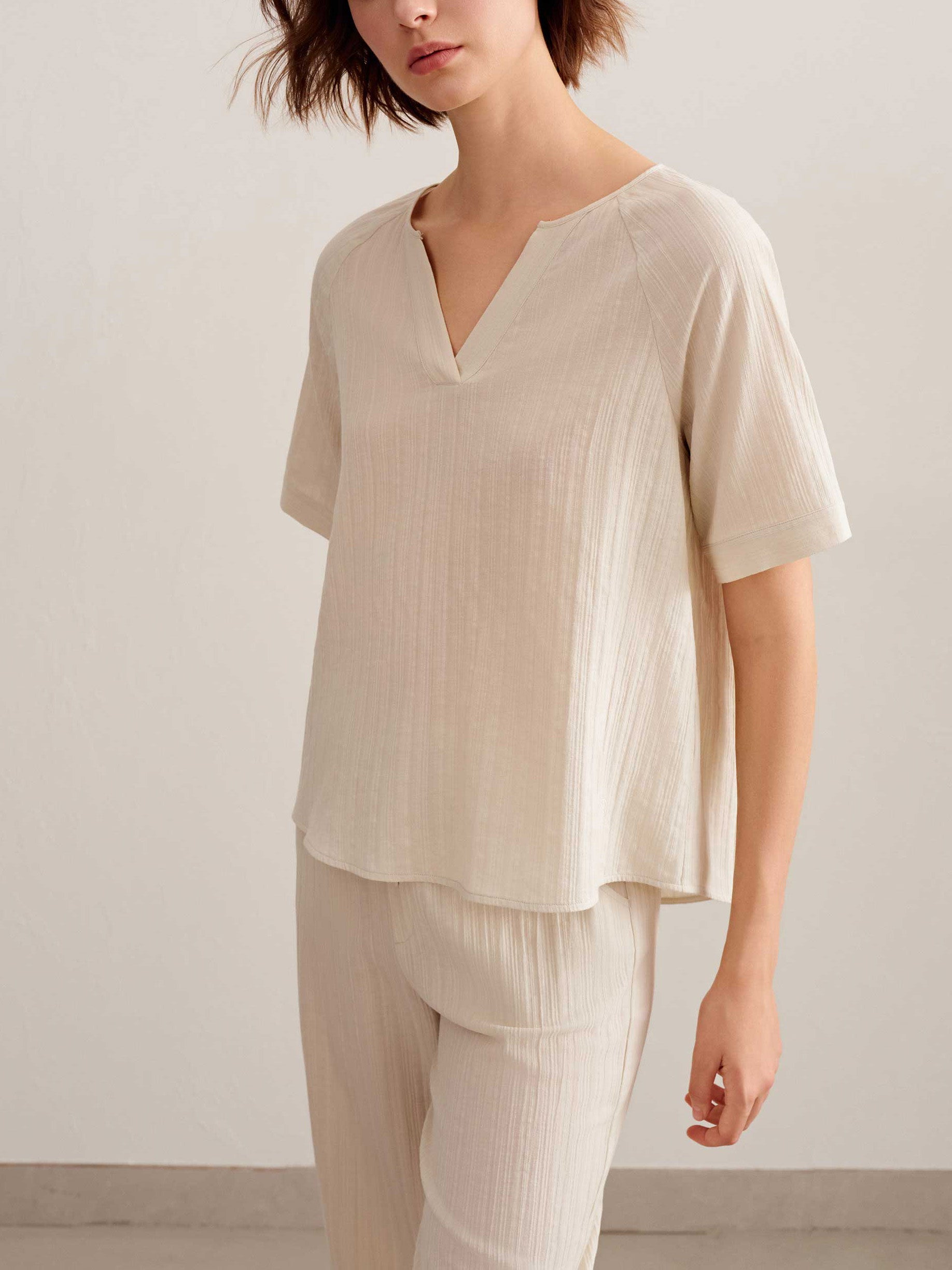 a woman wearing a light beige short sleeve v neckline tee and pants. 