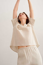 a woman lifts her arms up wearing a a woman wearing a light beige short sleeve tee and pants. 