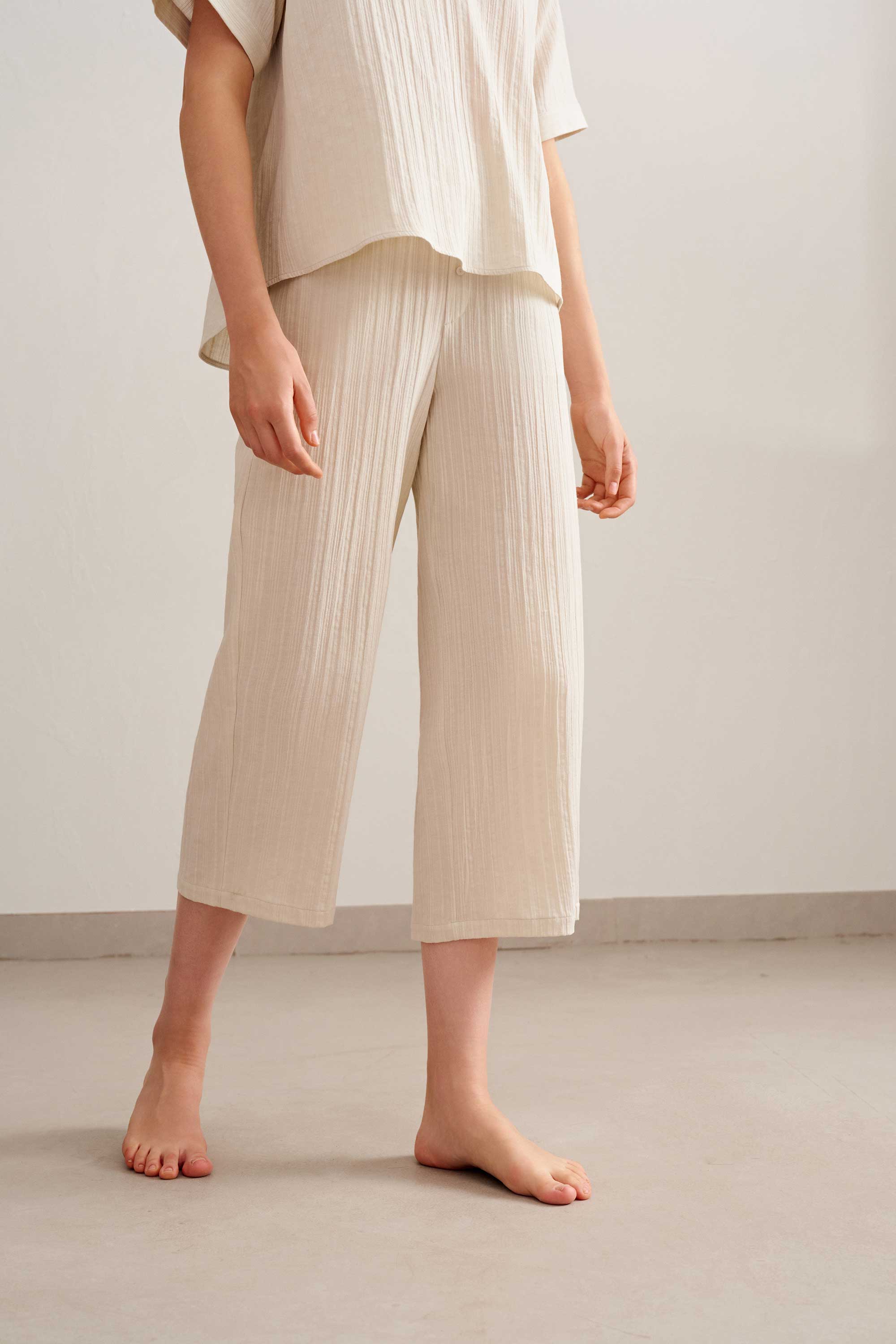 a woman wearing a light beige top and cropped pants.