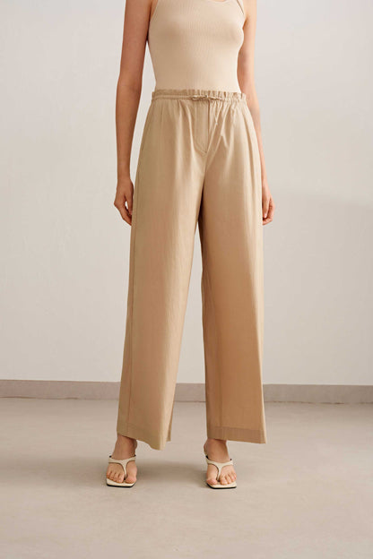 a woman wearing a beige tank tucked in light brown wide leg pants. pair with a white sandal. 