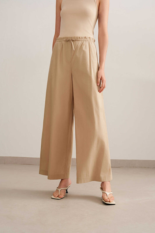 a women wearing a cream tank and light brown wide leg pants also a white sandal. 