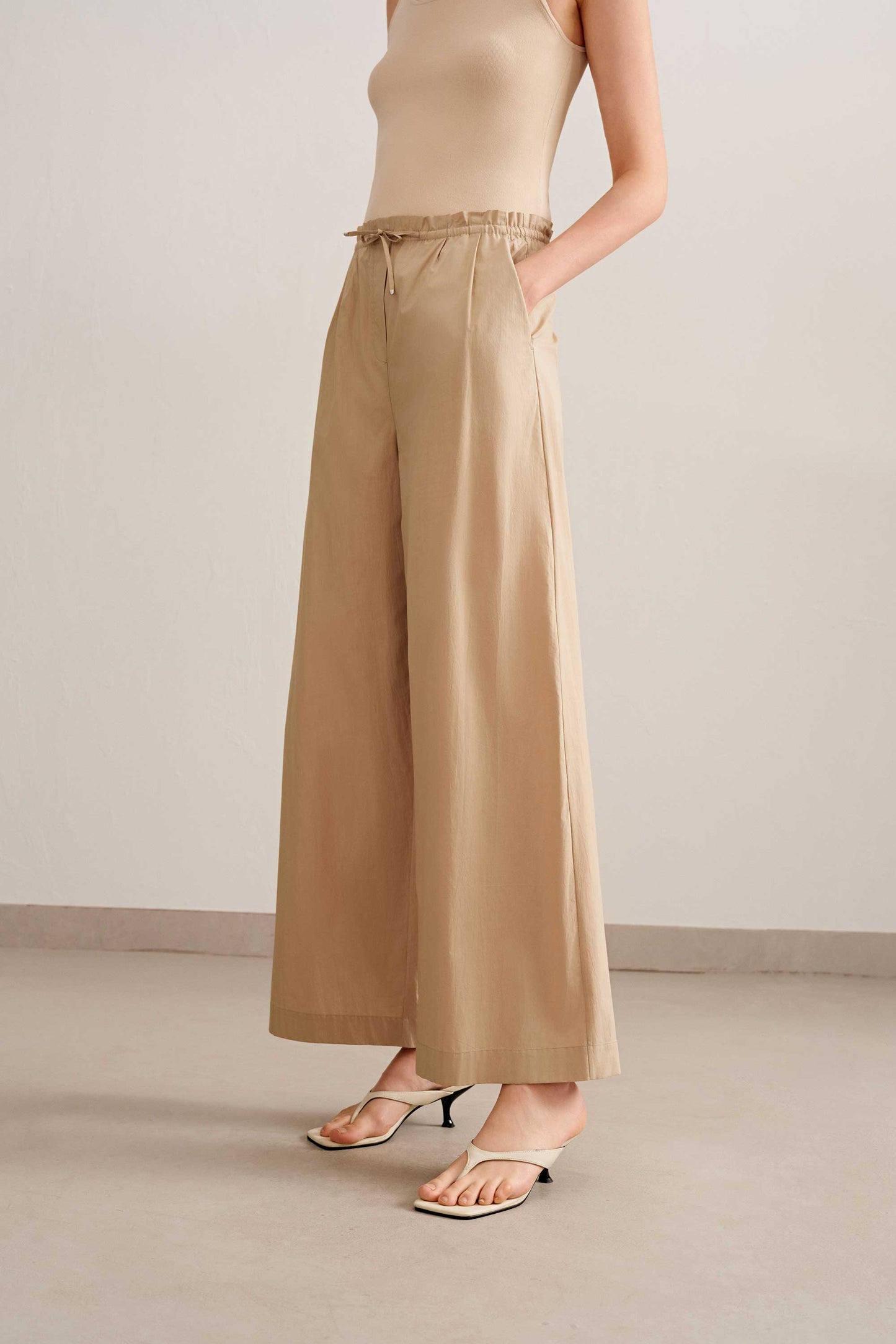 side look of a woman wearing a beige tank and light brown wide leg pants, pair with a white sandal. 