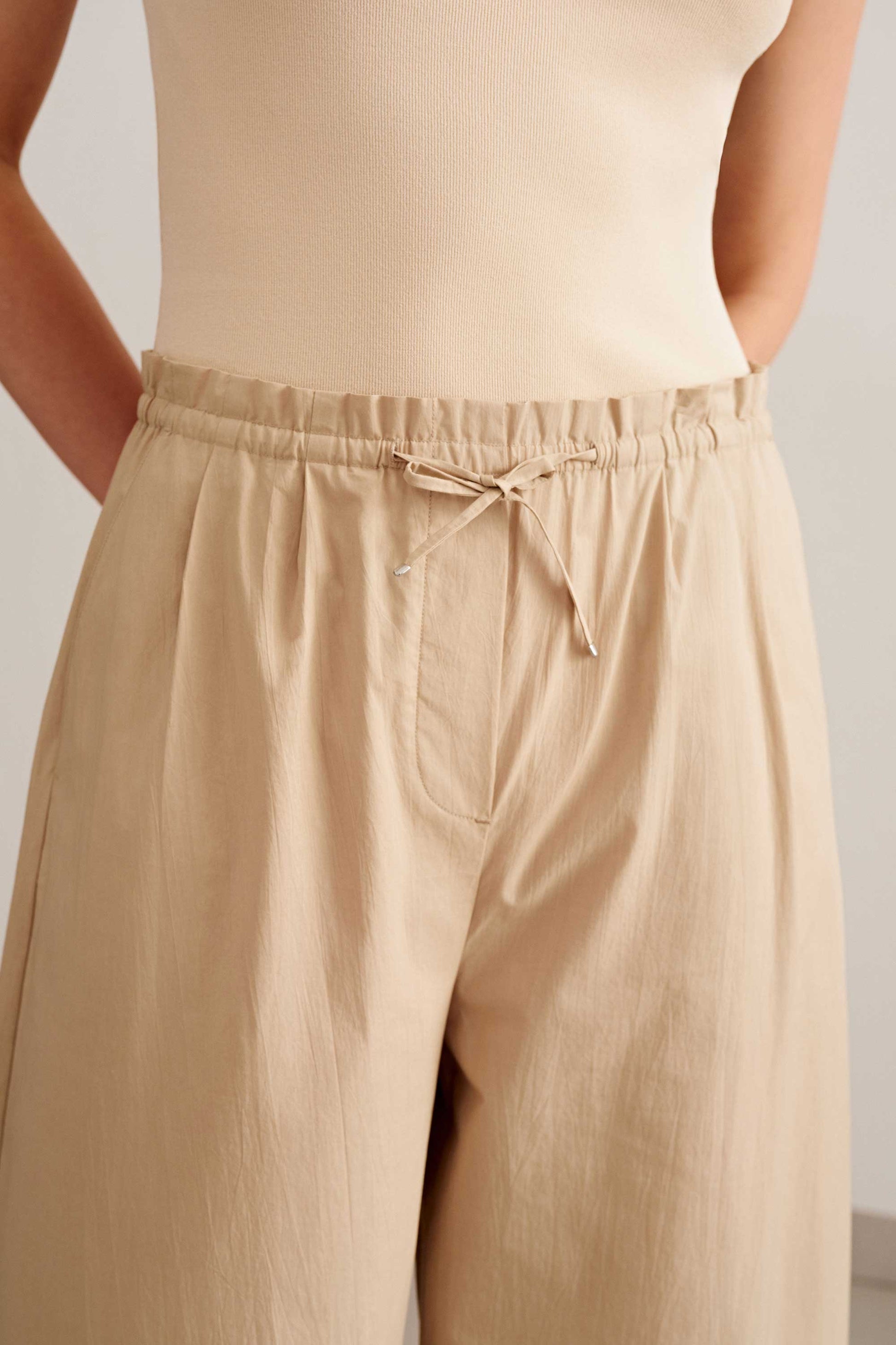 a woman wearing a top that tucked in light brown pants. the pants has a knot tying.  