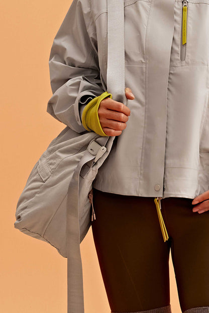 a woman wearing a grey jacket holding her grey bag