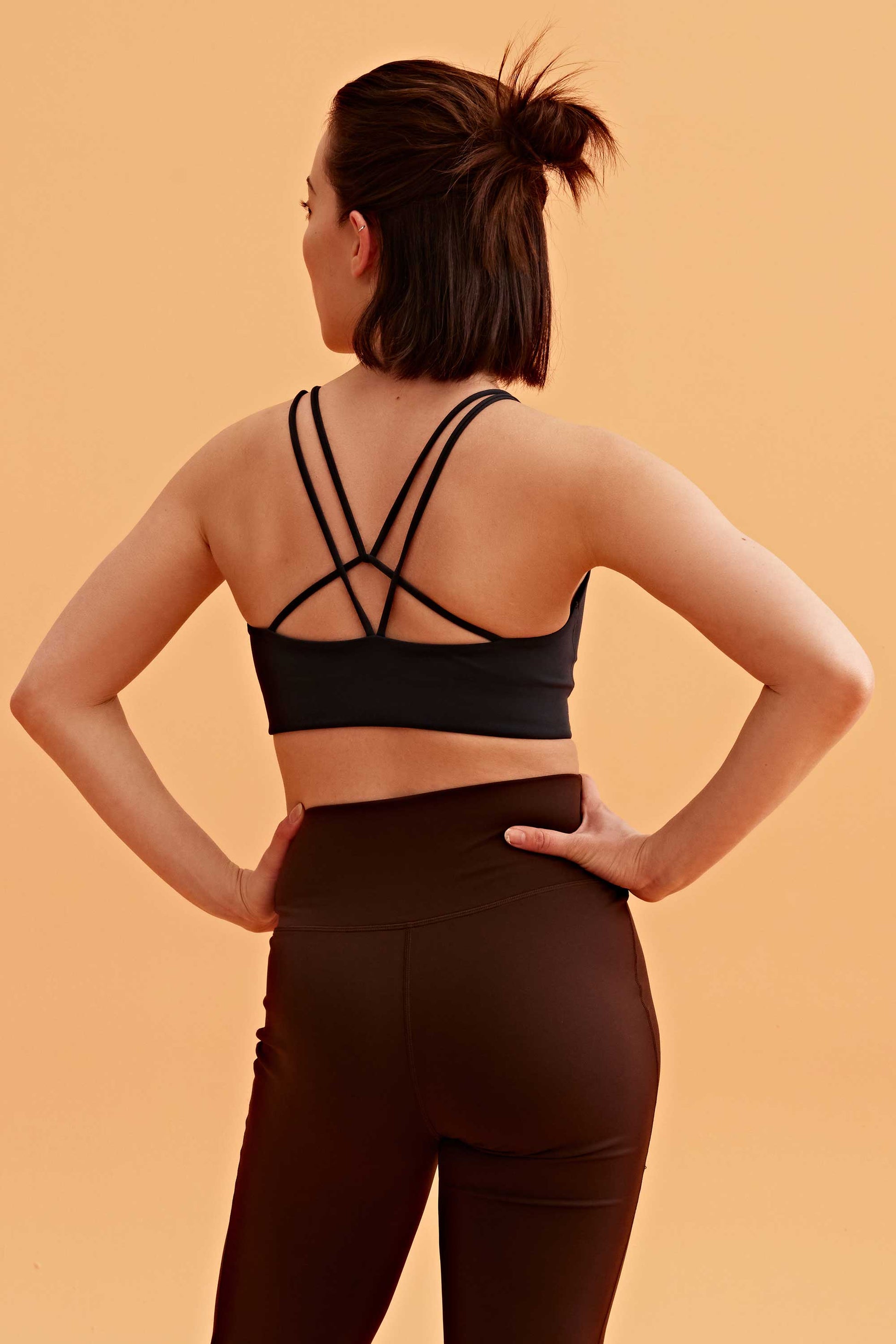 back of a woman wearing the black sports bra and brown pants. 