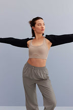 a woman open her arms wearing a black shrug and light grey sports bra and grey pants.