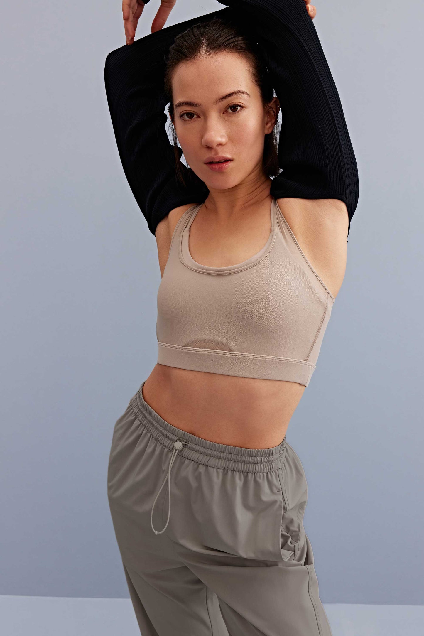 a woman wearing a black shrug and light grey sports bra and grey pants.