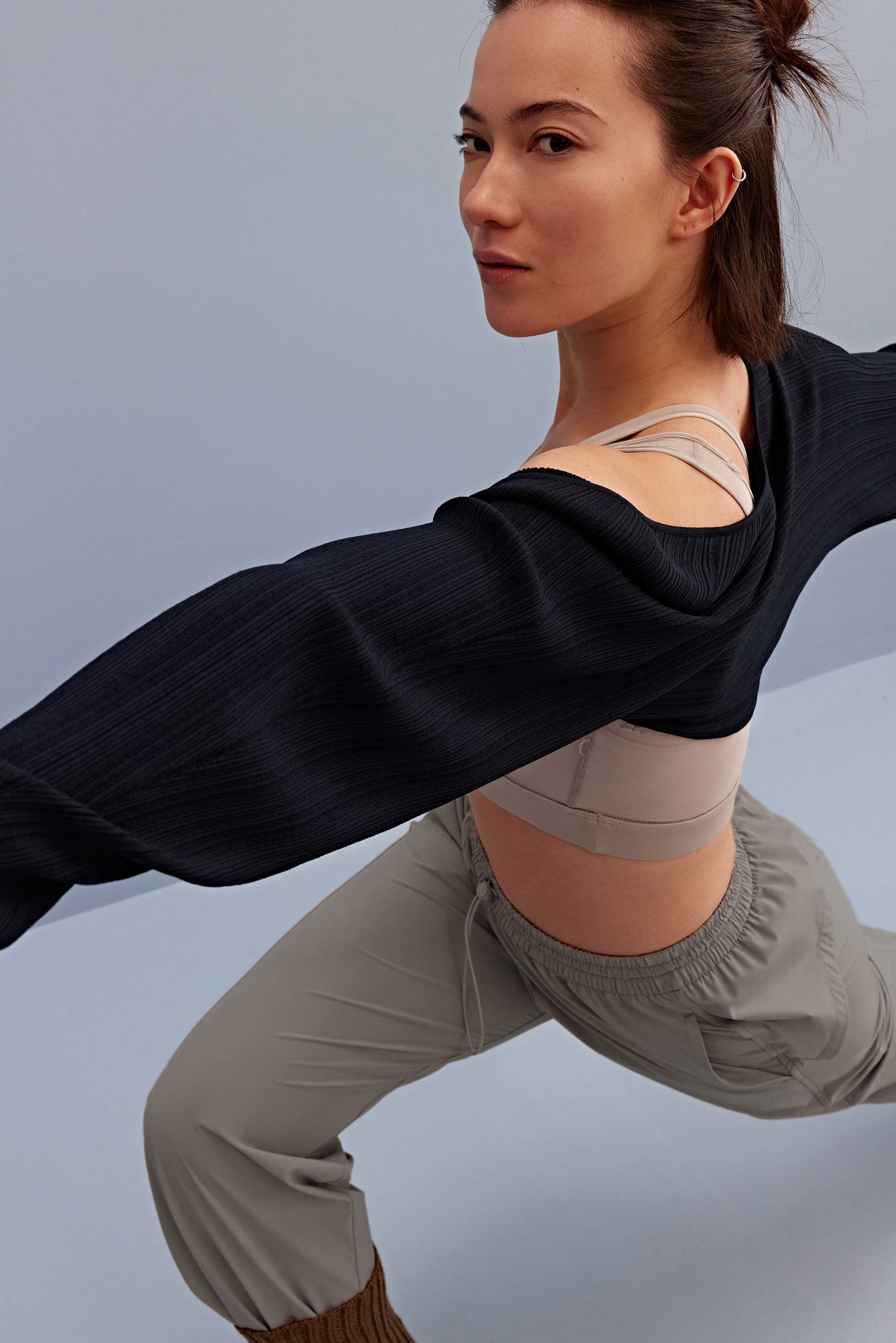 a woman wearing a light grey sports bra, black shrug and grey pants. 
