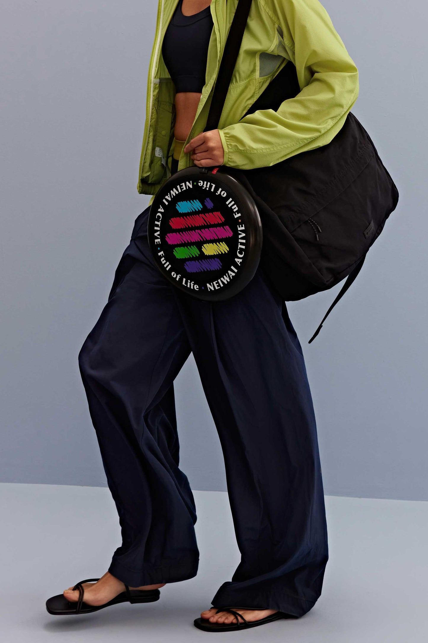 a woman wearing a green jacket and black sports bra, pair with navy pants and black bag