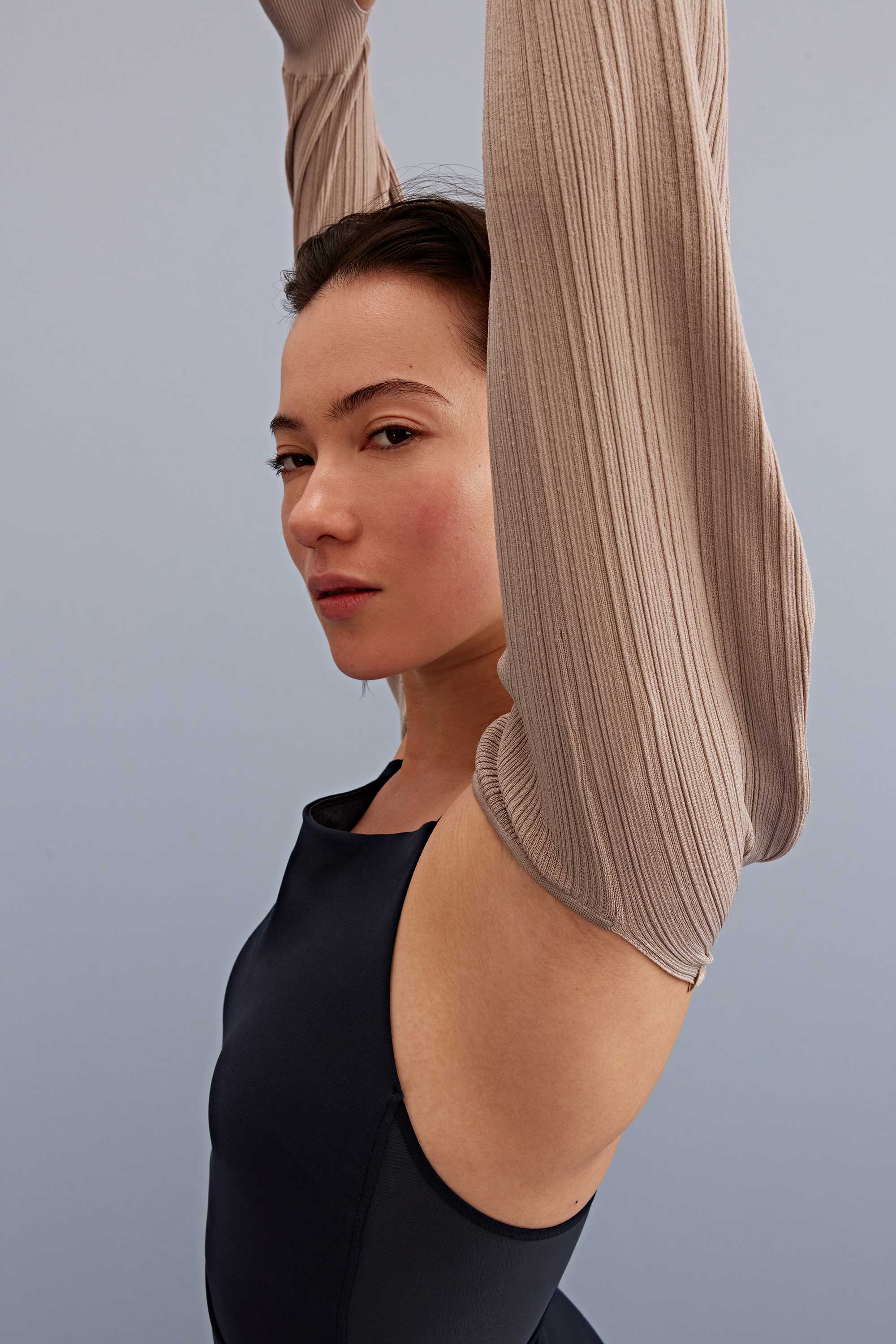 a woman put her arms up wearing a light brown shrug and black sports bra