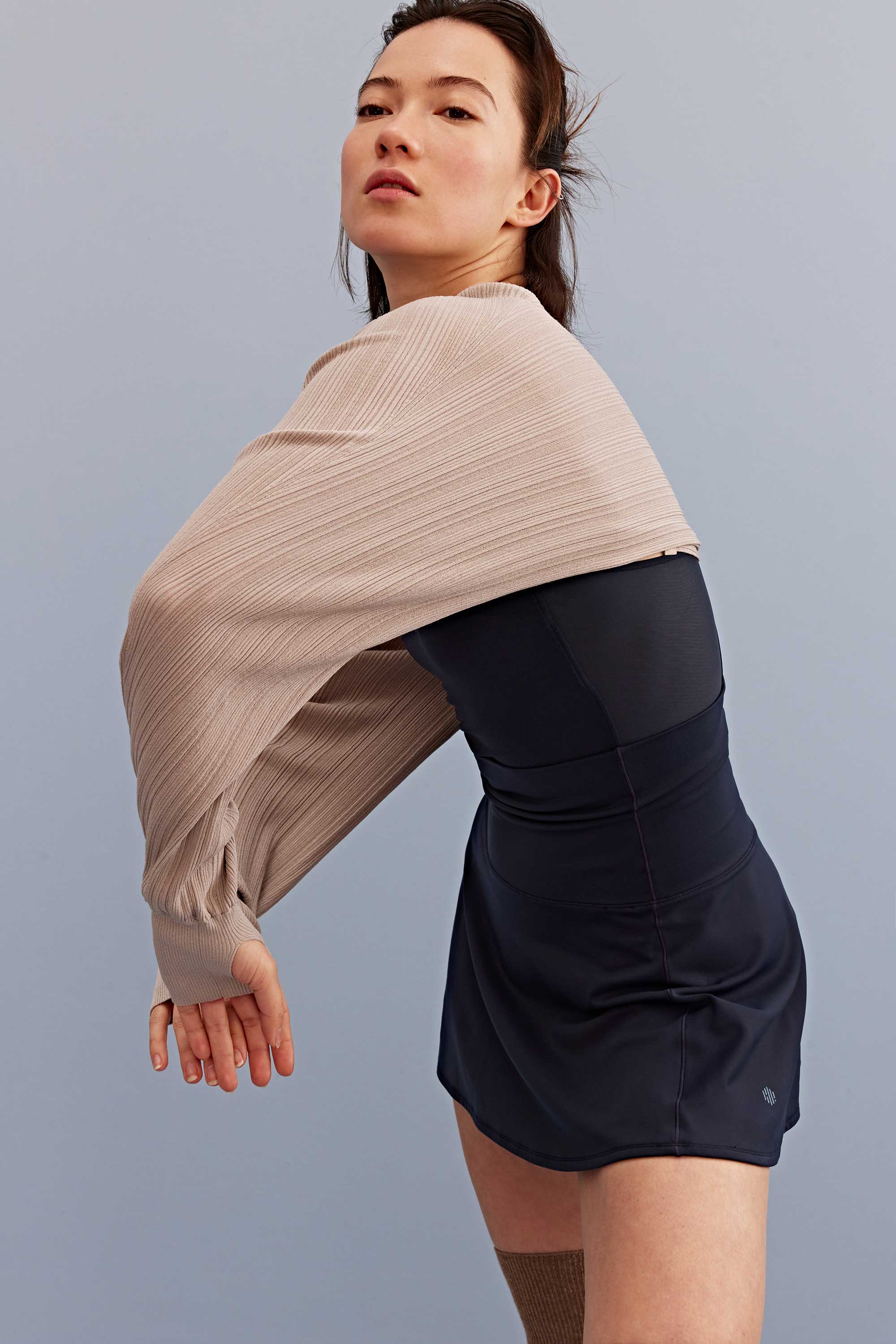 a woman wearing a light brown shrug and black sports bra and skirt. 