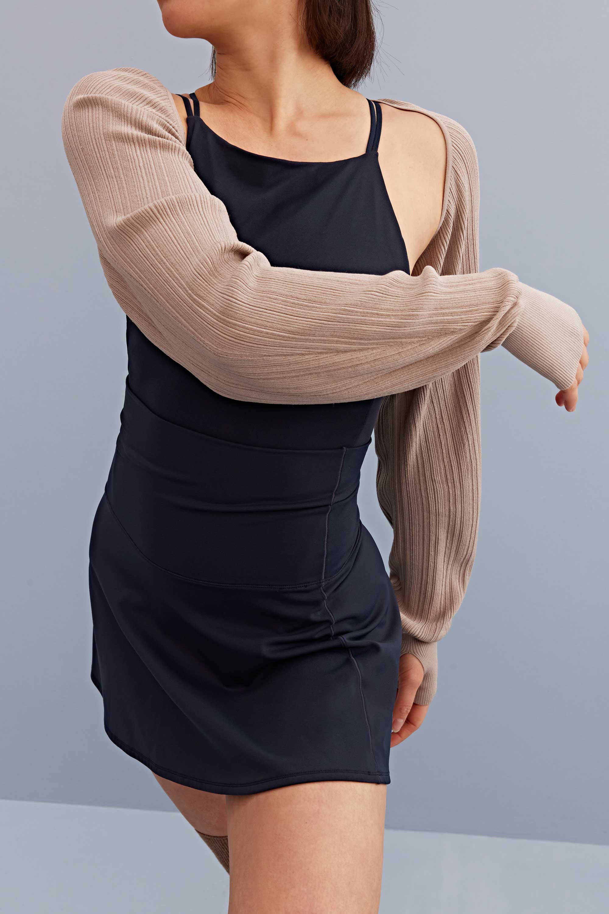 a woman wearing a light brown shrug with black sports bra and skirt. 