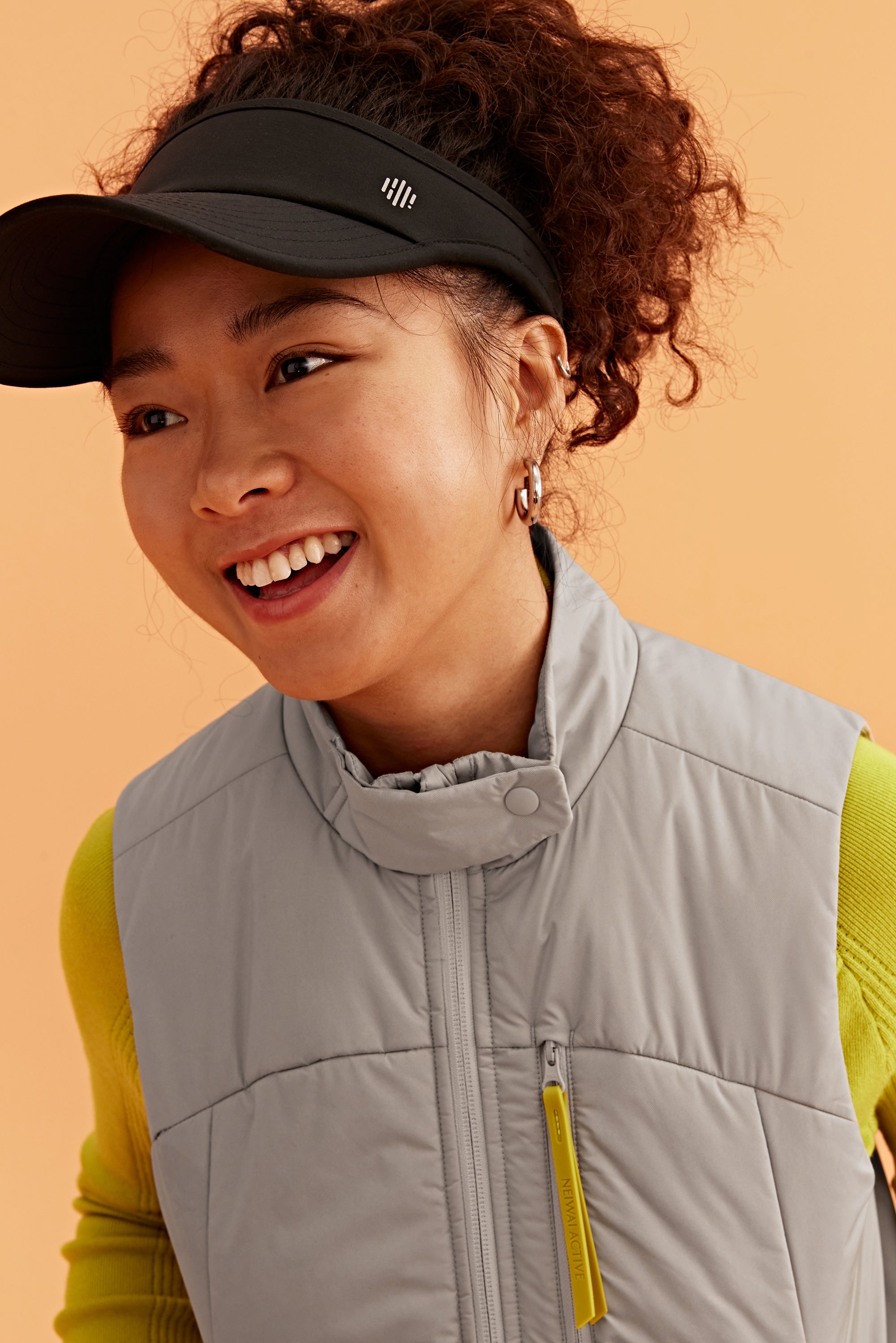 a woman wearing black visor and grey vest with green sweatshirt under