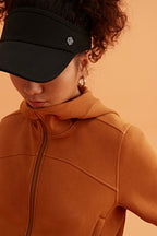 a woman looking down wearing a black visor and brown jacket
