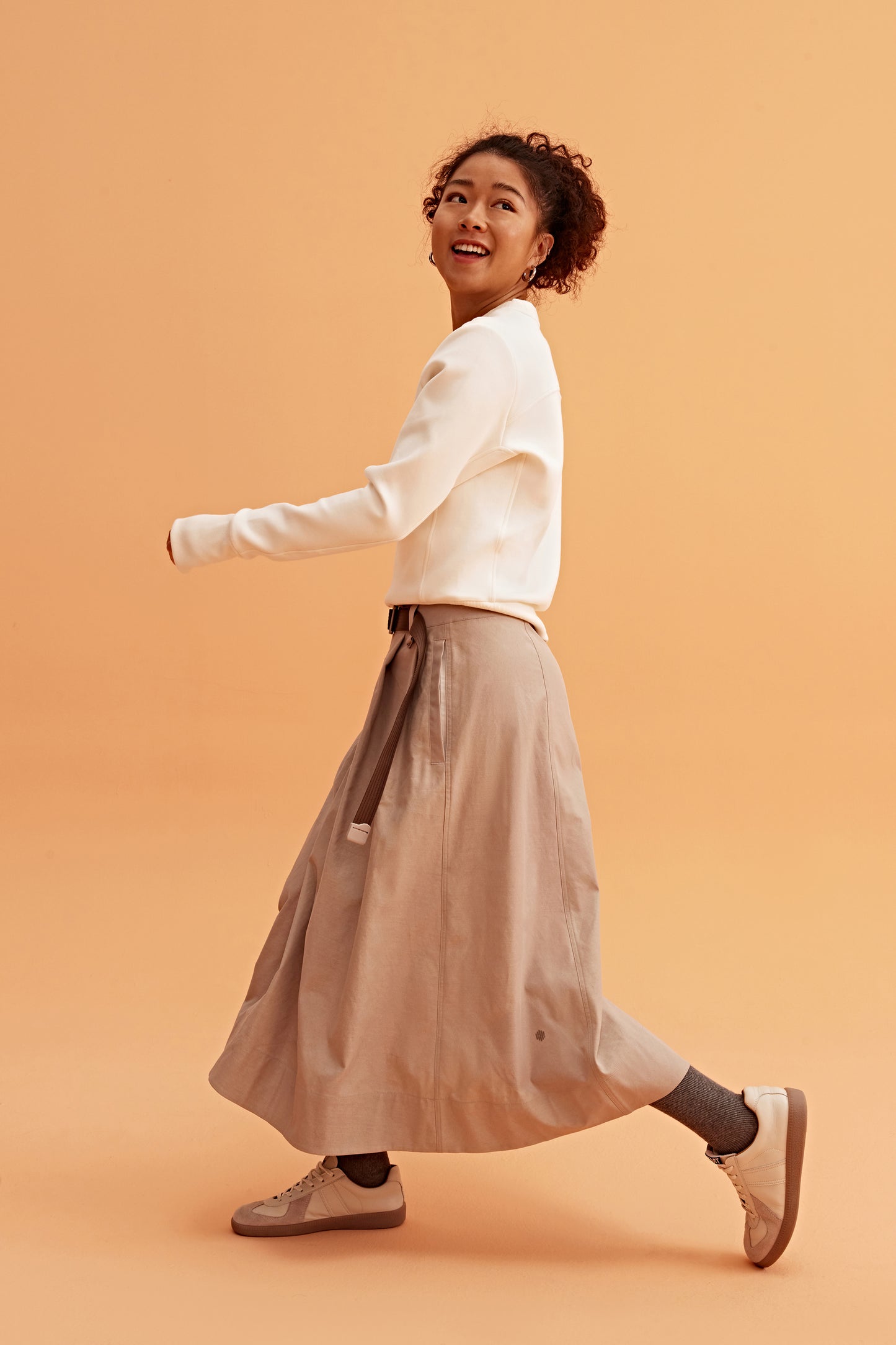 side of a woman wearing a white sweatshirt and brown skirts.
