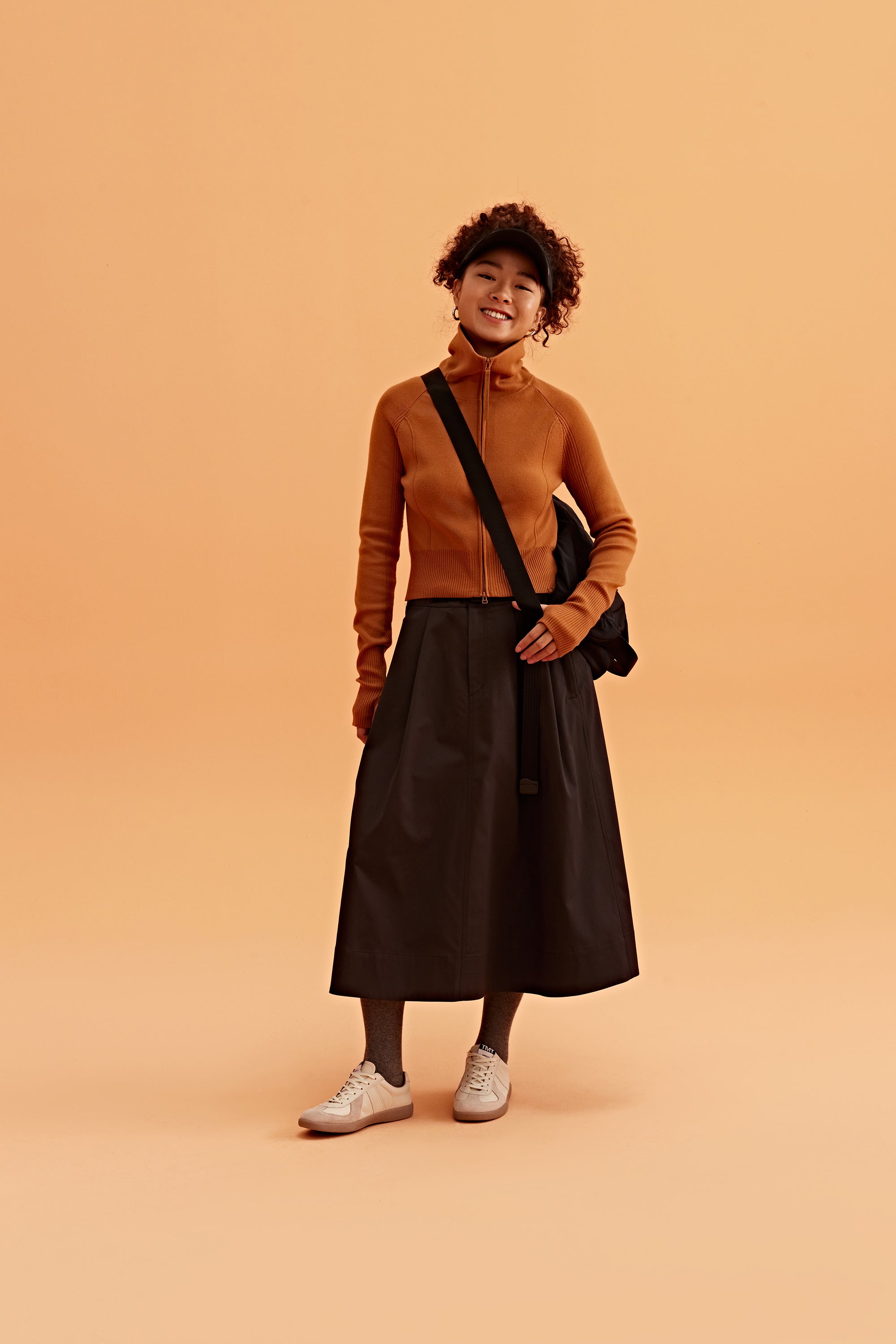 a woman wearing a black visor, brown cardigan brown skirt and black bag