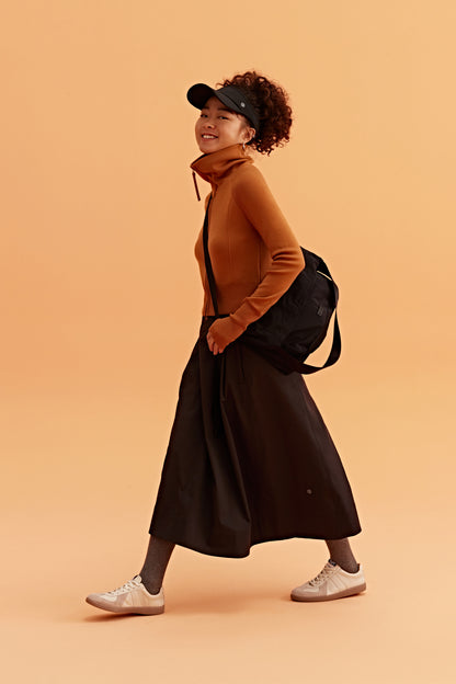 a woman wearing a black visor, brown cardigan brown skirt and black bag