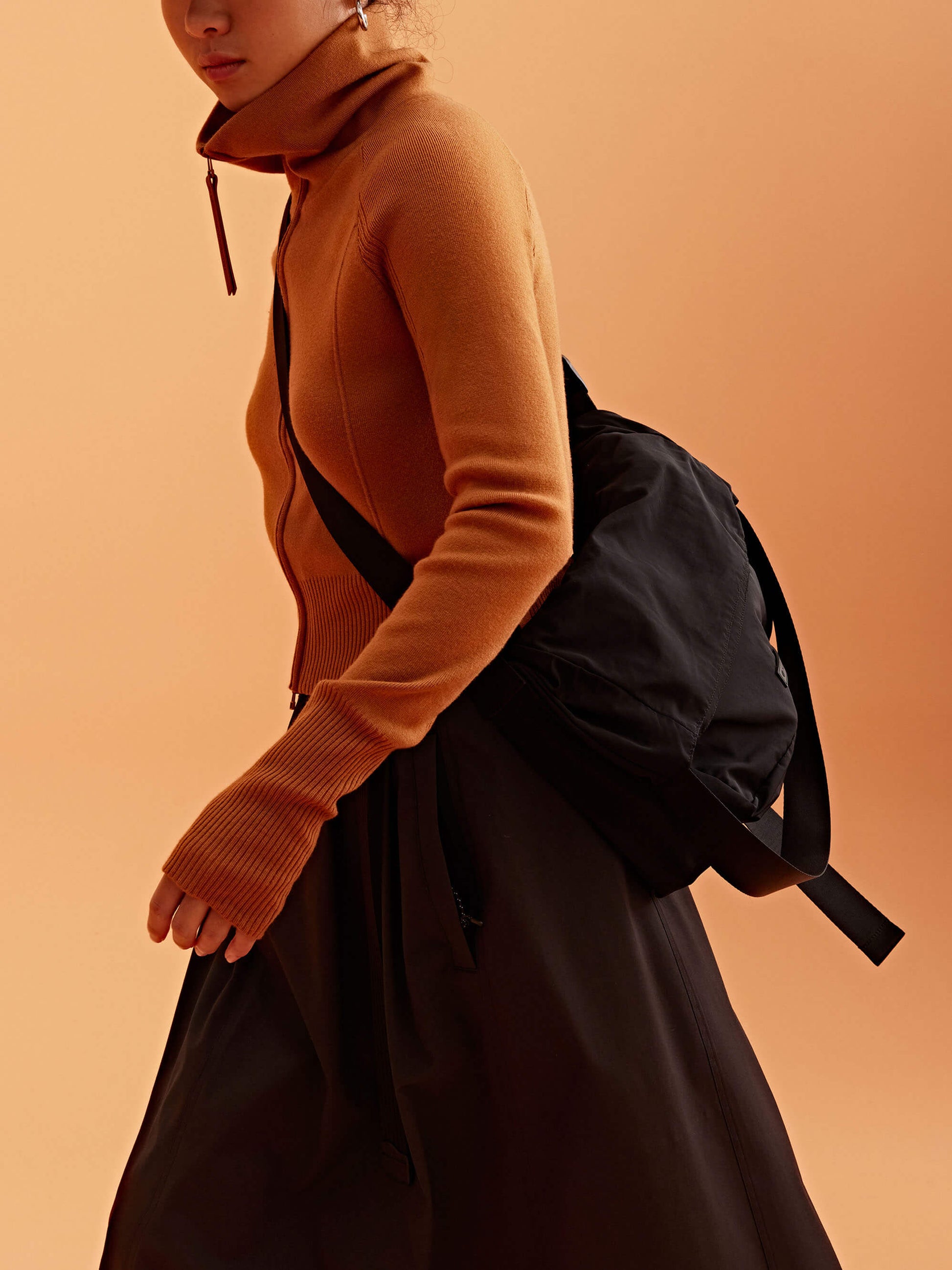 a woman wearing a black visor and brown cardigan, pair with black bag and brown skirt.