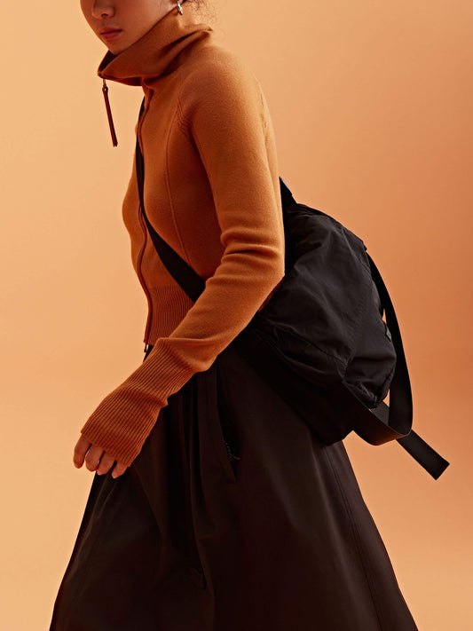 a woman wearing a black visor and brown cardigan, pair with black bag and brown skirt.