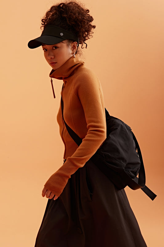 a woman wearing a black visor, brown cardigan  brown skirt and black bag