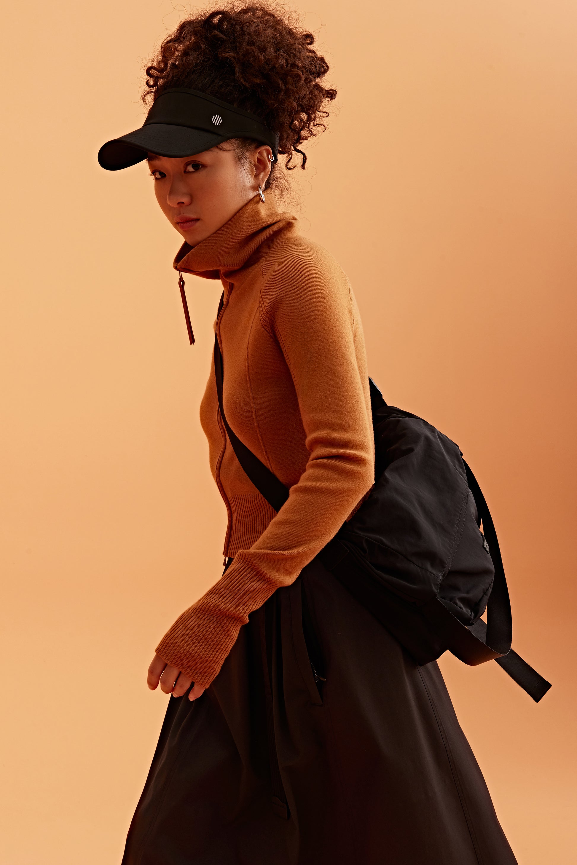 a woman wearing a black visor and brown cardigan, pair with black bag and brown skirt.