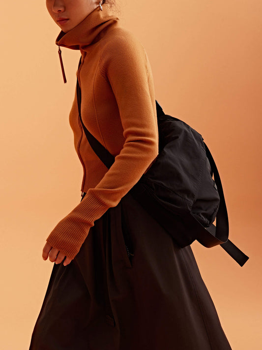 a woman wearing a black visor, brown cardigan  brown skirt and black bag