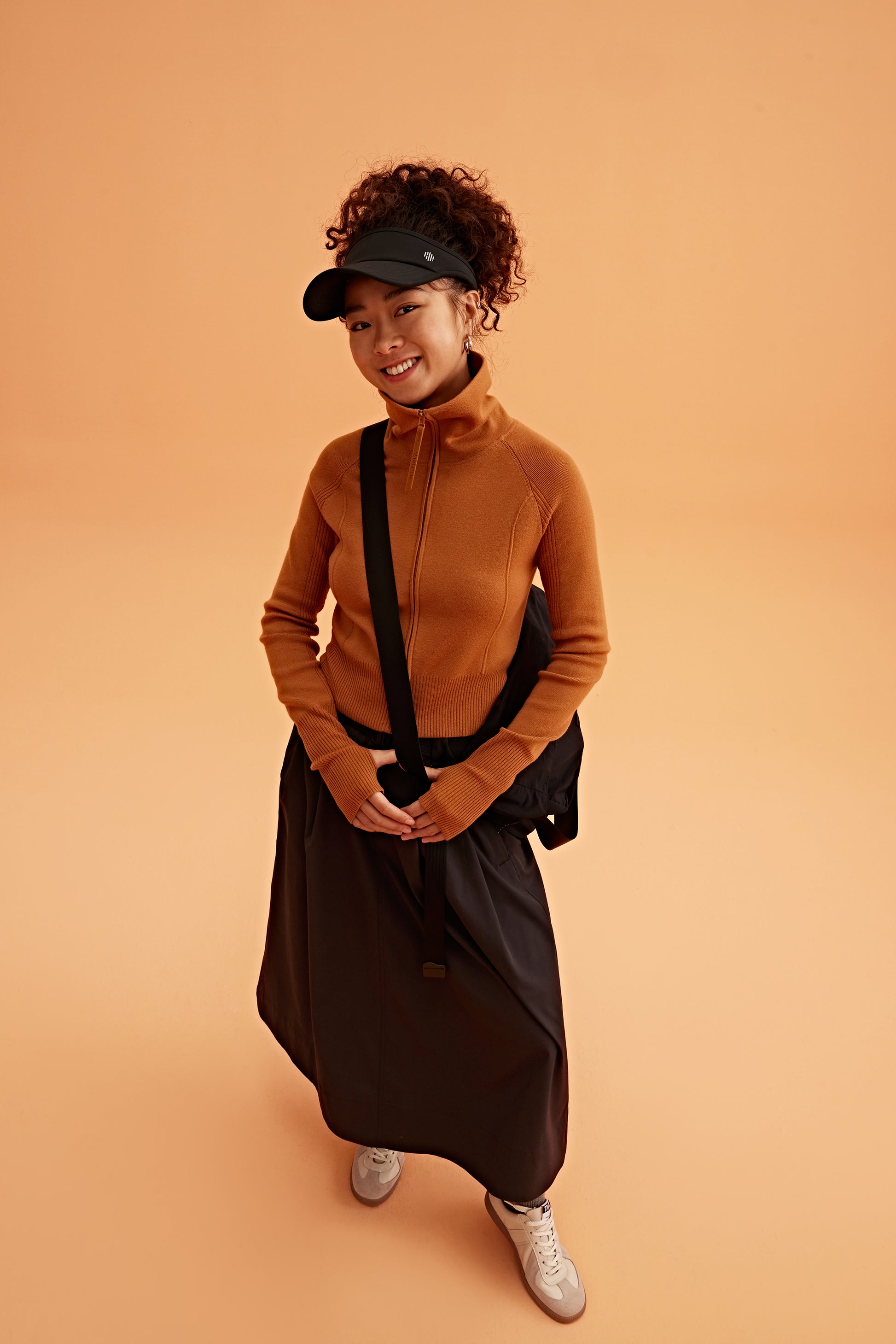 a woman wearing a black visor, brown cardigan brown skirt and black bag