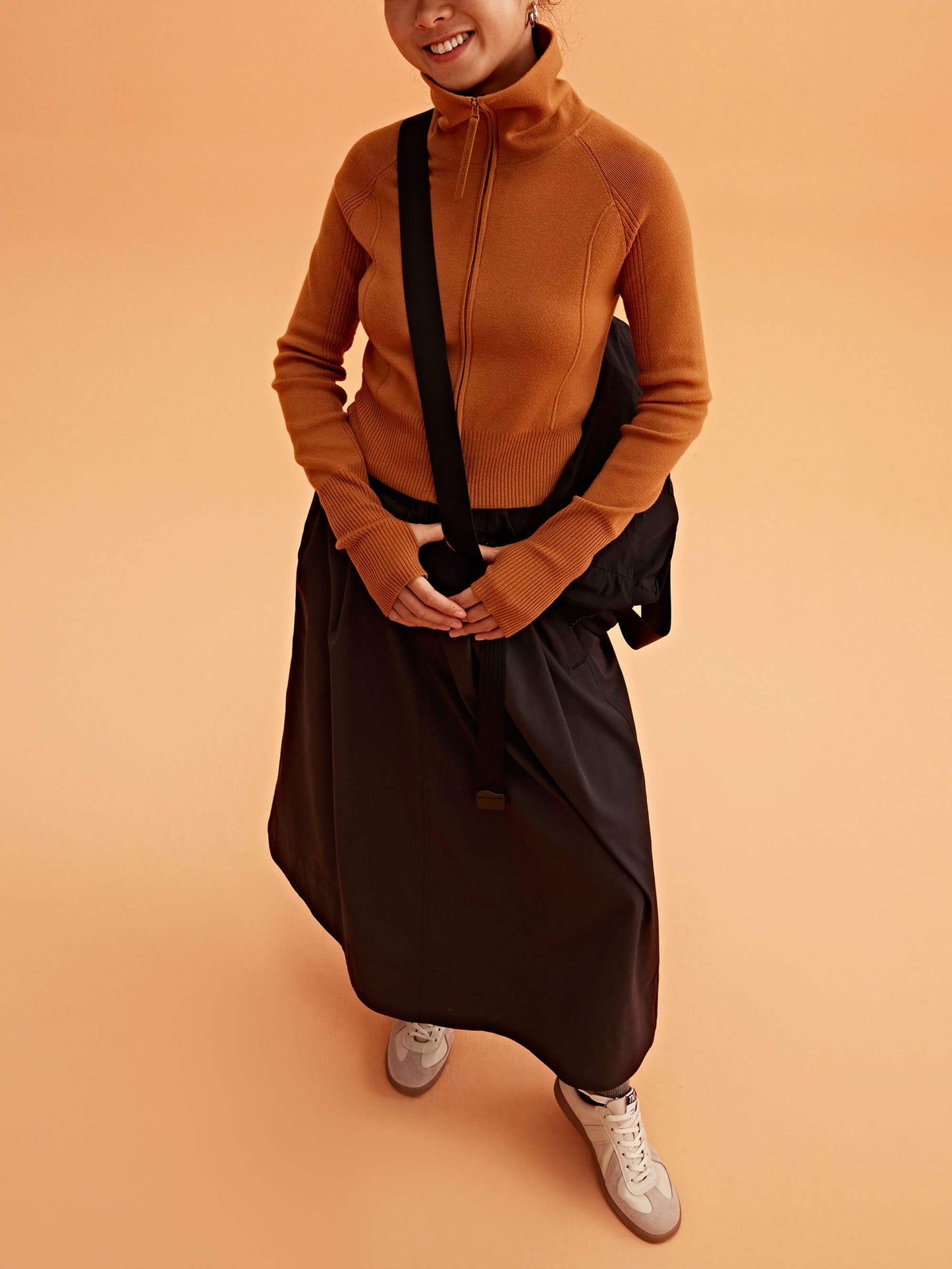 a woman wearing a black visor, brown cardigan brown skirt and black bag