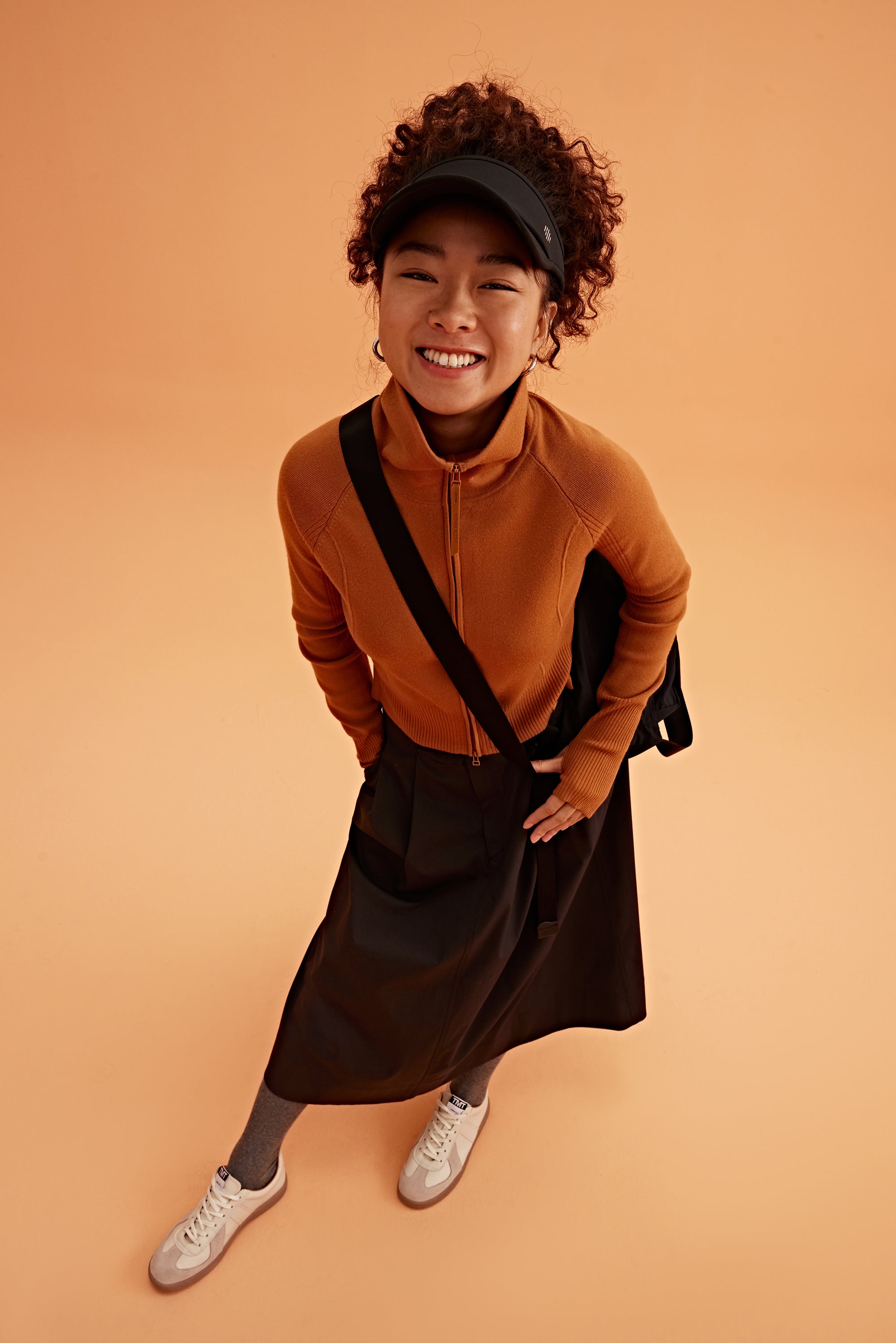 a woman wearing a black visor, brown cardigan brown skirt and black bag